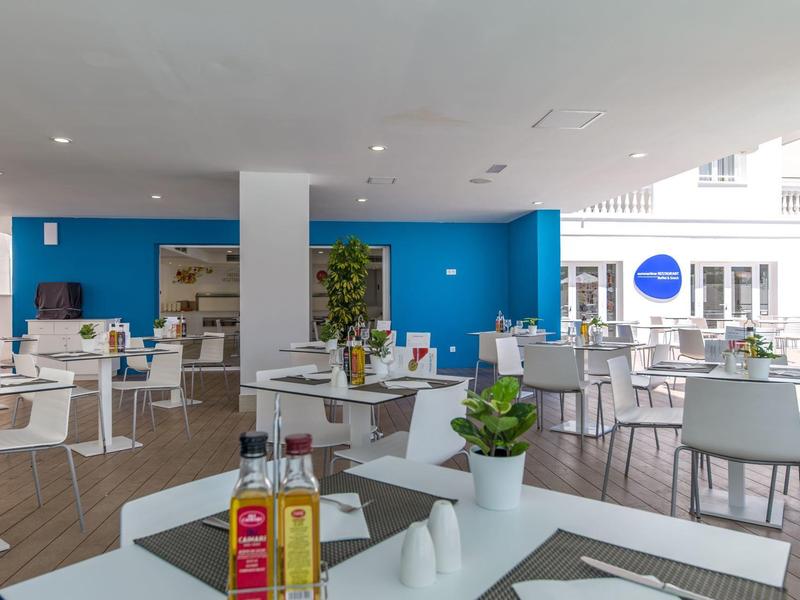 Area ristorante moderna dell'hotel con tavoli bianchi, sedie e parete blu.