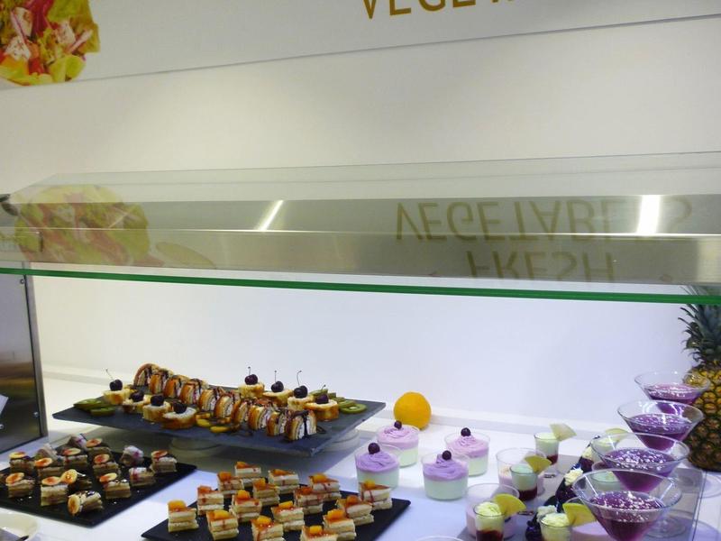 Banco con snack di verdure fresche e piccoli dolci sotto una copertura in vetro.