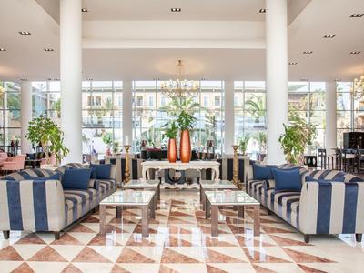 Heller, großzügiger Raum mit gestreiften Sofas, großen Fenstern, Pflanzen und Marmorboden.