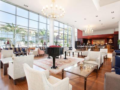 Bright hotel lobby with large windows, white armchairs, and a black grand piano.
