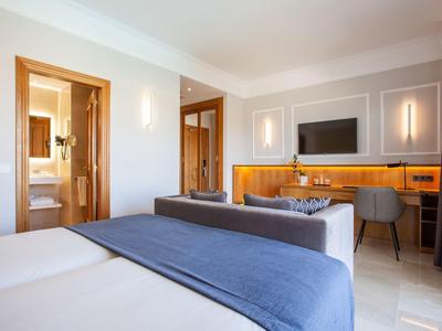 Modernes Hotelzimmer mit Doppelbett, Holzschreibtisch, Fernseher und Badezimmerzugang.