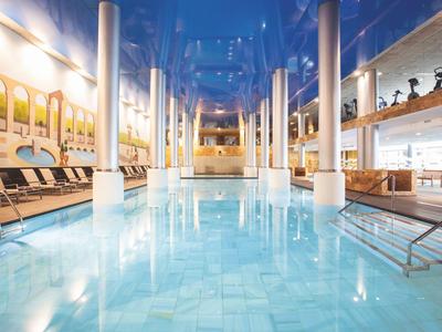 Bright indoor pool with comfortable lounge chairs and large windows, numerous columns in the room.