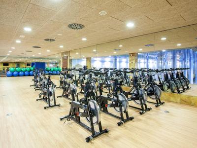 A fitness room with multiple stationary bikes on a wooden floor and large mirrors on the wall.