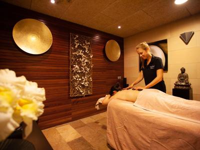 Ein Wellnessraum mit Holzdecke, warmen Farben und einer Frau bei einer Massage.