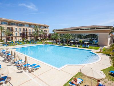 Large outdoor pool with sun loungers and hotels in the background on a sunny day.