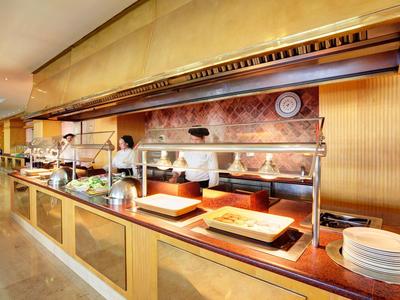 Buffet mit warmen Speisen, Holztheke, Tellerstapel und Küchenpersonal im Hintergrund.