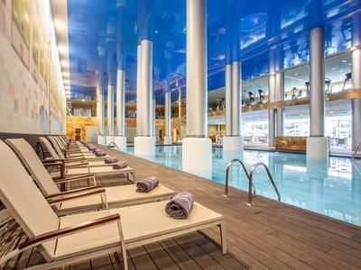 Luxuriöser Innenpool mit braunen Liegestühlen, weißen Säulen und glänzendem blauem Deckendetail.