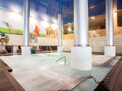 Moderner Innenpool mit Holzdeck, weißen Säulen und großen Wandbildern im Hintergrund.