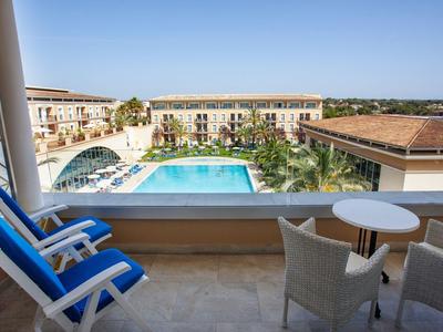 Balkon mit blauem Stuhl, Tisch, Ausblick auf Hotel mit großem Pool und klarem Himmel.