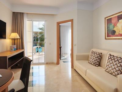 Helles, modernes Zimmer mit Sofa, Fernseher, Schreibtisch, Tür zum Balkon und hellem Boden.