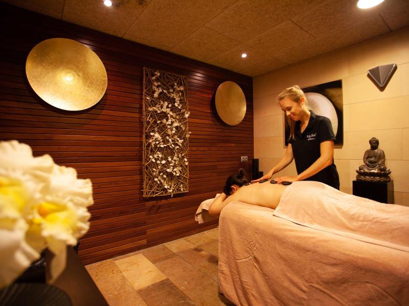 Ein Wellnessraum mit Holzdecke, warmen Farben und einer Frau bei einer Massage.