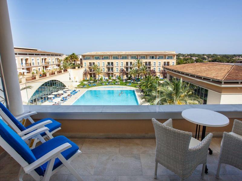 Balkon mit blauem Stuhl, Tisch, Ausblick auf Hotel mit großem Pool und klarem Himmel.