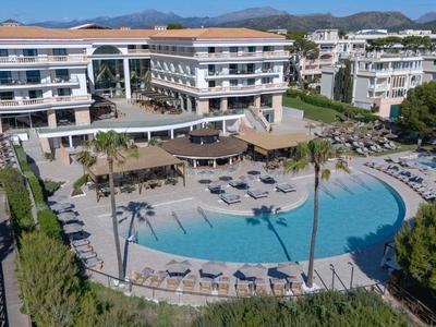 Gran piscina con tumbonas rodeada de hoteles y árboles verdes en un resort vacacional.