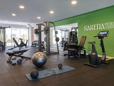 Gimnasio moderno con equipo de entrenamiento, pesas y pared verde para huéspedes del hotel.
