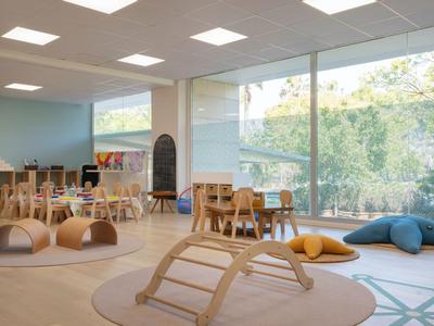 Sala de juegos infantil luminosa y moderna con juguetes de madera y grandes ventanas con vista a la vegetación.