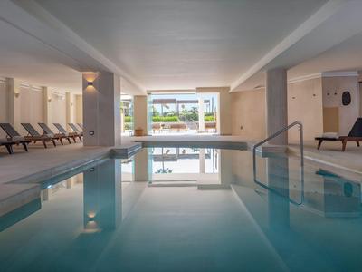 Piscina interior de hotel con tumbonas y paredes claras.