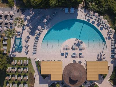 Piscina redonda de hotel con sombrillas y tumbonas, rodeada de vegetación.