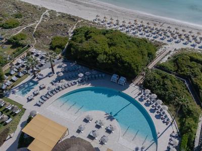 Vista aérea de un hotel con una gran piscina y una playa con sombrillas.