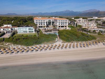 Hotel de playa con filas de sombrillas en la playa de arena y montañas al fondo.