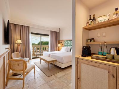 Habitación de hotel luminosa con cama doble, zona de estar y balcón con vistas al mar.