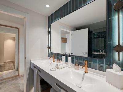 Baño de hotel bien iluminado con dos lavabos y un gran espejo.