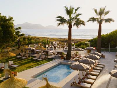 Hotel pool with lounge chairs and umbrellas next to palm trees overlooking the sea.