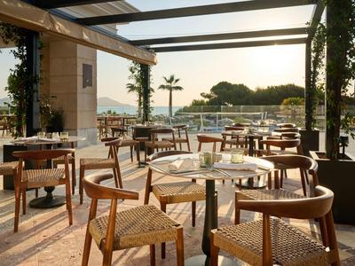 Restauracja na świeżym powietrzu z drewnianymi meblami i widokiem na port o zachodzie słońca.