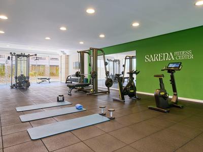 Modern gym room with mats, weights, and machines against a green hotel wall.