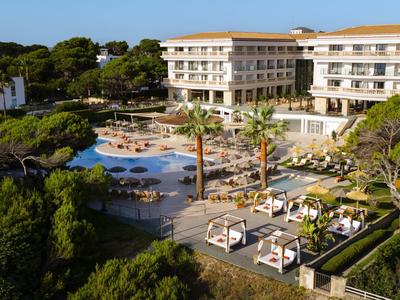 Duży hotel z basenem, leżakami i bujną roślinnością w spokojnej okolicy.