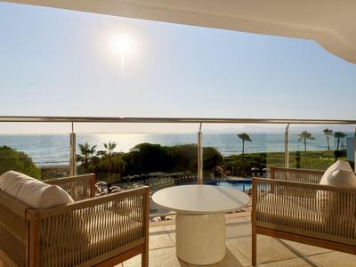 Balcón con dos sillas, mesa y vista al mar al amanecer o al atardecer.