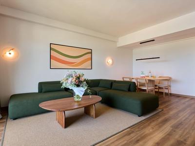 Sala de estar moderna con sofá verde, mesa de madera y área de comedor al fondo.