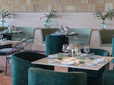 Restaurante elegante con sillas de terciopelo verde y mesas preparadas en un hotel.