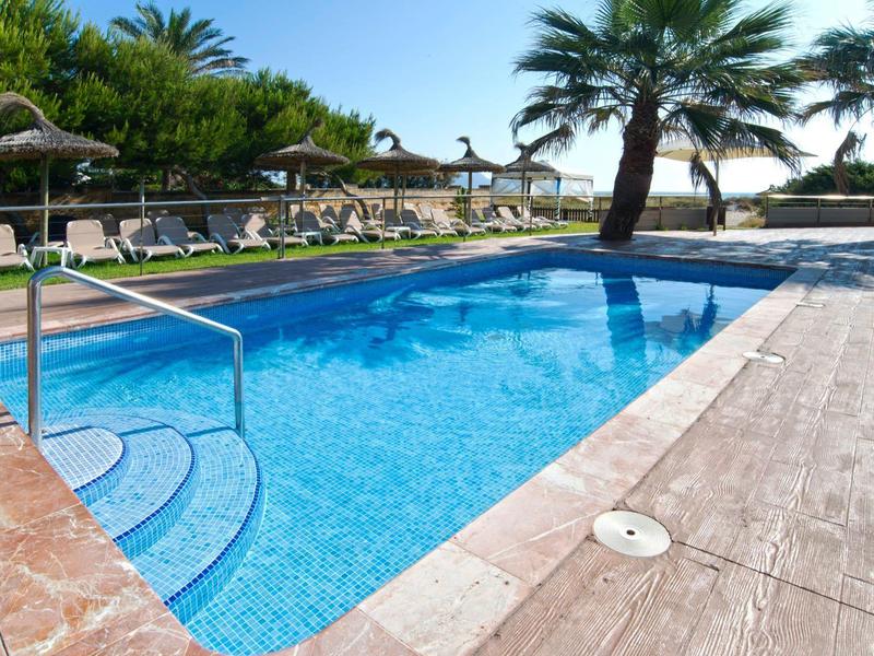 Mały basen z schodami, otoczony parasolami i palmami w ośrodku hotelowym.