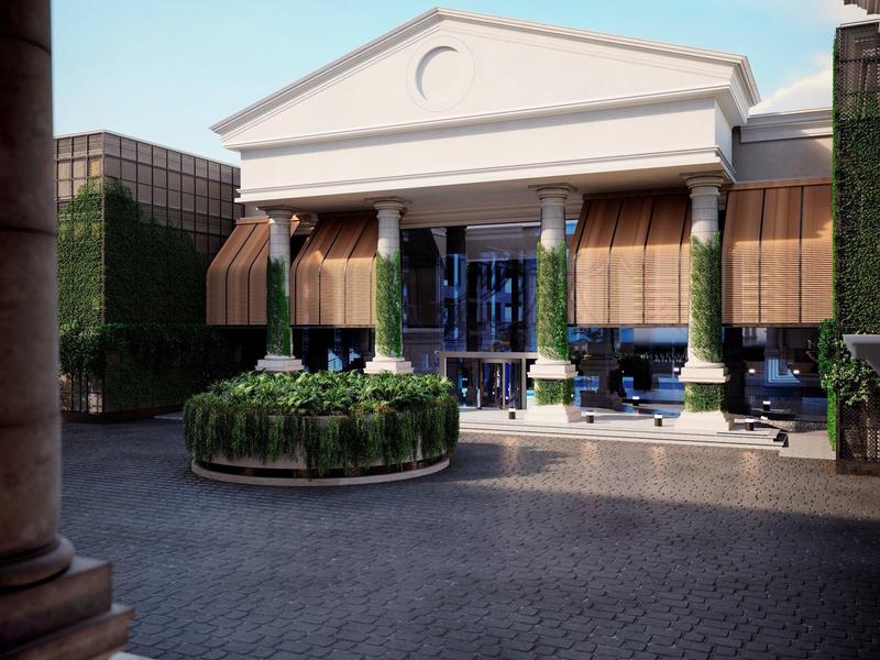 Dziedziniec hotelu z klasyczną fasadą, kolumnami i okrągłą roślinnością pod jasnym niebem.