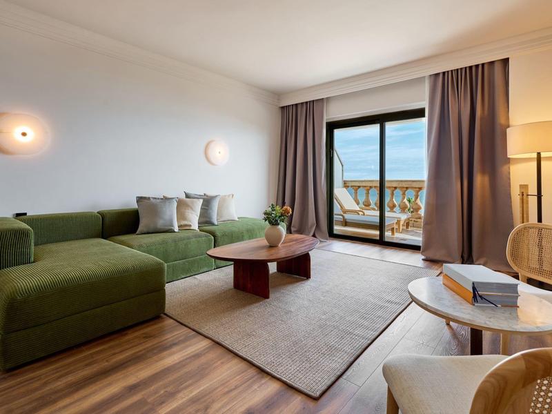 Przytulny salon z zieloną sofą, drewnianą podłogą i widokiem na balkon i morze.