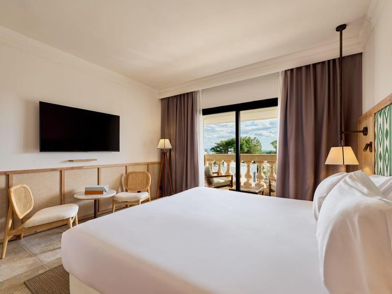 Pokój hotelowy z dużym łóżkiem, telewizorem, miejscem do siedzenia i balkonem z widokiem na morze.