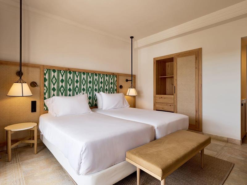 Nowoczesny pokój hotelowy z dwoma łóżkami, stolikami nocnymi i drewnianymi meblami.