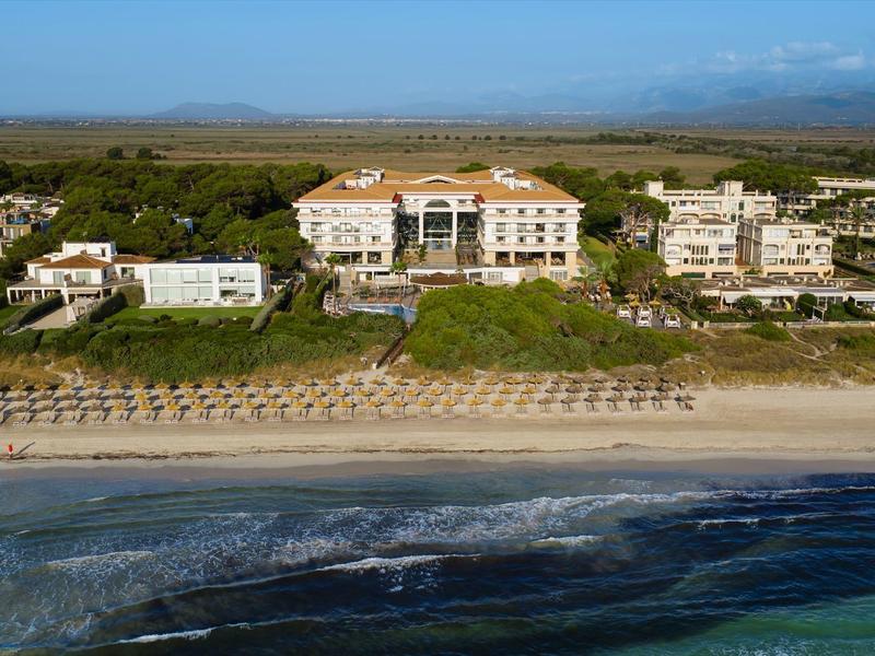 Widok na plażę z parasolami i hotelami w tle pod jasnym niebem.