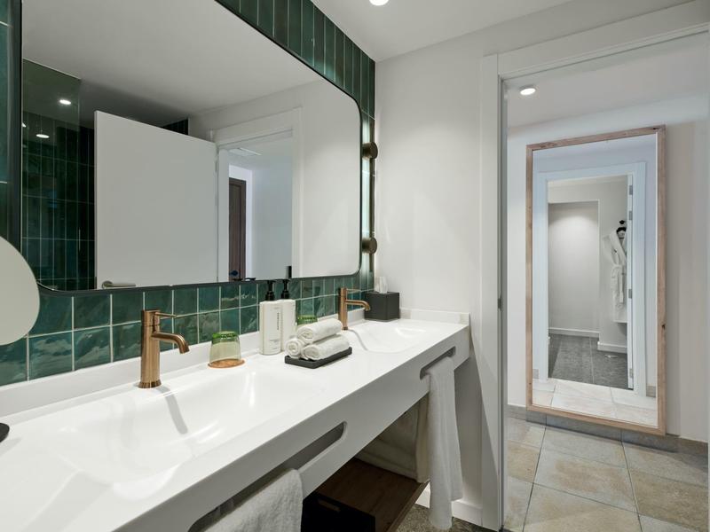 Nowoczesna łazienka z białą umywalką, dużym lustrem i zielonymi kafelkami na ścianie.