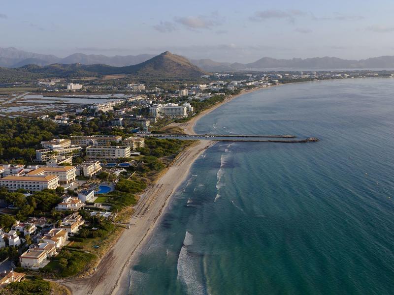 Zdjęcie lotnicze nadmorskiego miasta z plażą, falami i budynkami przy wybrzeżu.