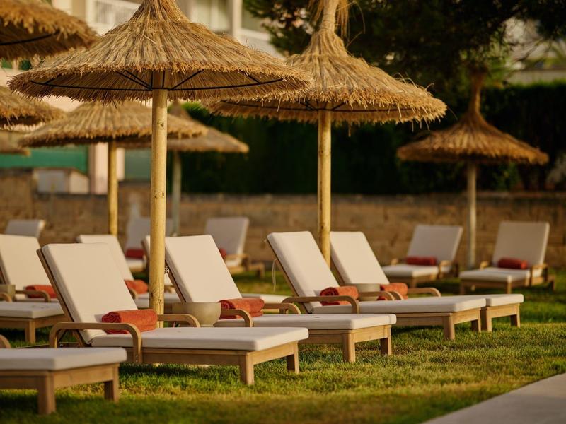 Leżaki z czerwonymi ręcznikami pod słomianymi parasolami na trawniku obok hotelu.