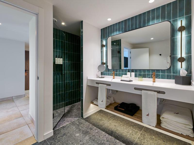 Nowoczesna łazienka z dużym lustrem, podwójną umywalką i zielonymi płytkami.