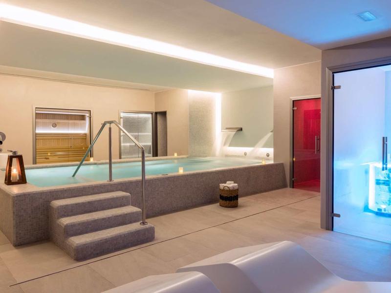 Area wellness moderna con piscina, scale e doccia illuminata in una stanza elegante.