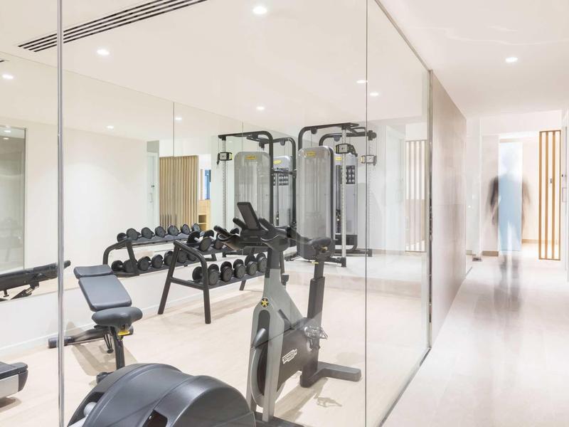 Palestra moderna con attrezzature da allenamento e manubri in un interno luminoso dell'hotel.