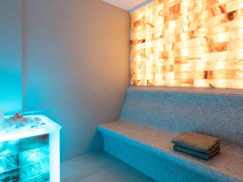 Grotta di sale moderna con pannello murale in pietra di sale illuminato e area salotto grigia.