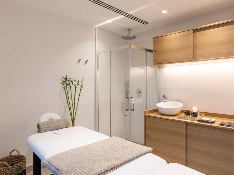 Stanza benessere semplice e luminosa con lettino da massaggio, cabina doccia e armadi in legno.