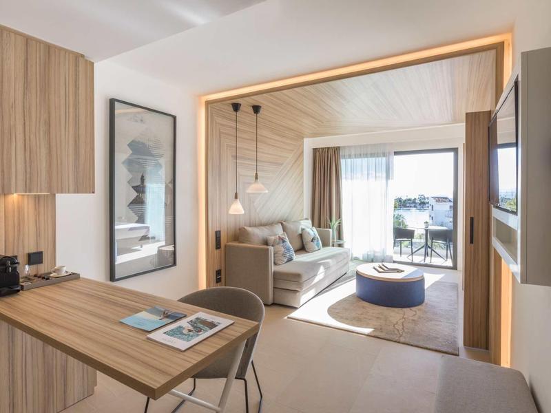 Camera d'albergo moderna con scrivania, divano e balcone con vista sul mare.