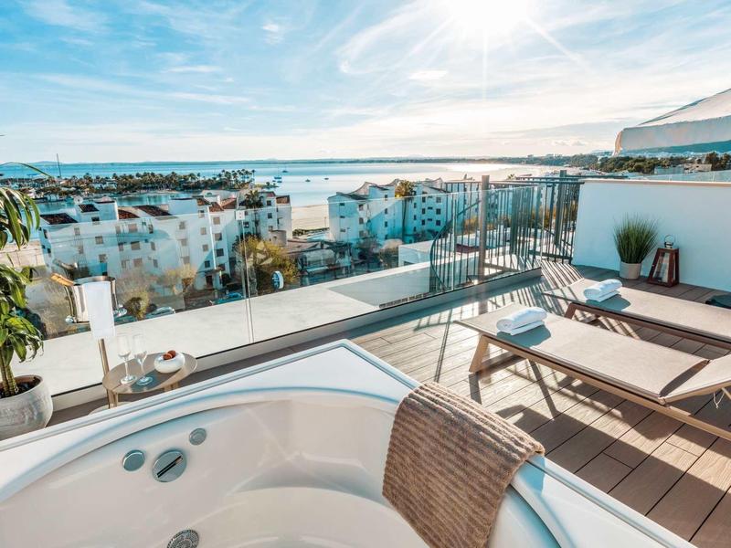 Terrazza sul tetto con vasca idromassaggio, lettini e vista sulla città e sul mare sotto il sole.