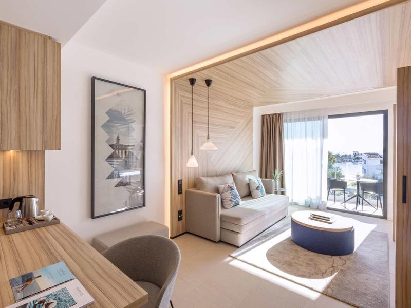 Camera d'hotel luminosa con angolo salotto, scrivania e balcone con vista mare.