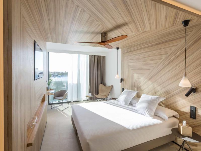 Camera d'hotel moderna con letto grande, pannelli in legno e balcone con vista.